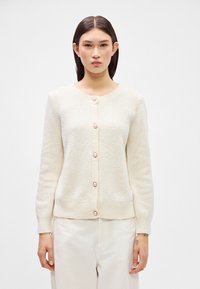 Lichtbeige gebreide cardigan met een ronde halslijn, lange mouwen en vijf parelachtige knopen aan de voorkant voor sluiting.