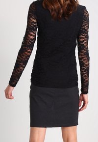 Czarny top z długimi koronkowymi rękawami, ozdobiony teksturowanym kwiatowym wzorem. Dopasowana szara spódnica. Pokazano widok od tyłu.