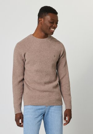Pull à côtes beige avec un col rond et des manches raglan, fabriqué à partir d'un matériau doux, associé à un jean en denim bleu clair.