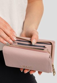 Portafoglio in pelle rosa con finitura tessurizzata, dotato di accessori dorati e due scomparti con zip. All'interno, sono visibili due slot per carte e un rivestimento in tessuto.