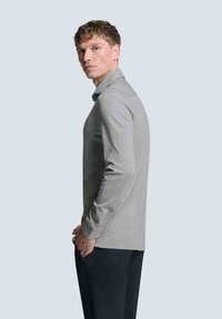 Graues Langarmshirt mit Kragen, im Slim-Fit geschnitten und mit seitlichen Schlitzen, kombiniert mit dunklen Hosen. Gleiche Textur und minimalistisches Design.