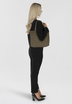 Olivgrüne, gesteppten Tragetasche mit strukturierter Form, doppelten Trägern und strukturierter Oberfläche, kombiniert mit einem schwarzen Outfit und hohen Schuhen.