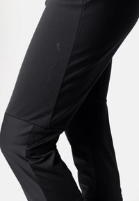 Pantalons de sport ajustés noirs en tissu lisse et résistant à l'étirement, avec un détail de logo subtil et un design effilé pour la mobilité.