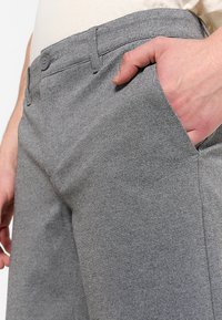 Gray trousers made of textured fabric, feature button closure, angled pockets, and a fitted design. Hand placed in pocket for detail.
