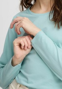 Svetlo modrá long-sleeve košeľa s okrúhlym výstrihom a priliehavými manžetami. Hladká bavlnená tkanina s jemnými švovými detailami, ruky upravujúce rukávy.