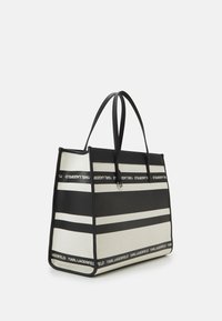 Sac fourre-tout rayé noir et crème en toile avec des poignées robustes en cuir noir et des détails de marque le long du bord sup érieur et de la base.