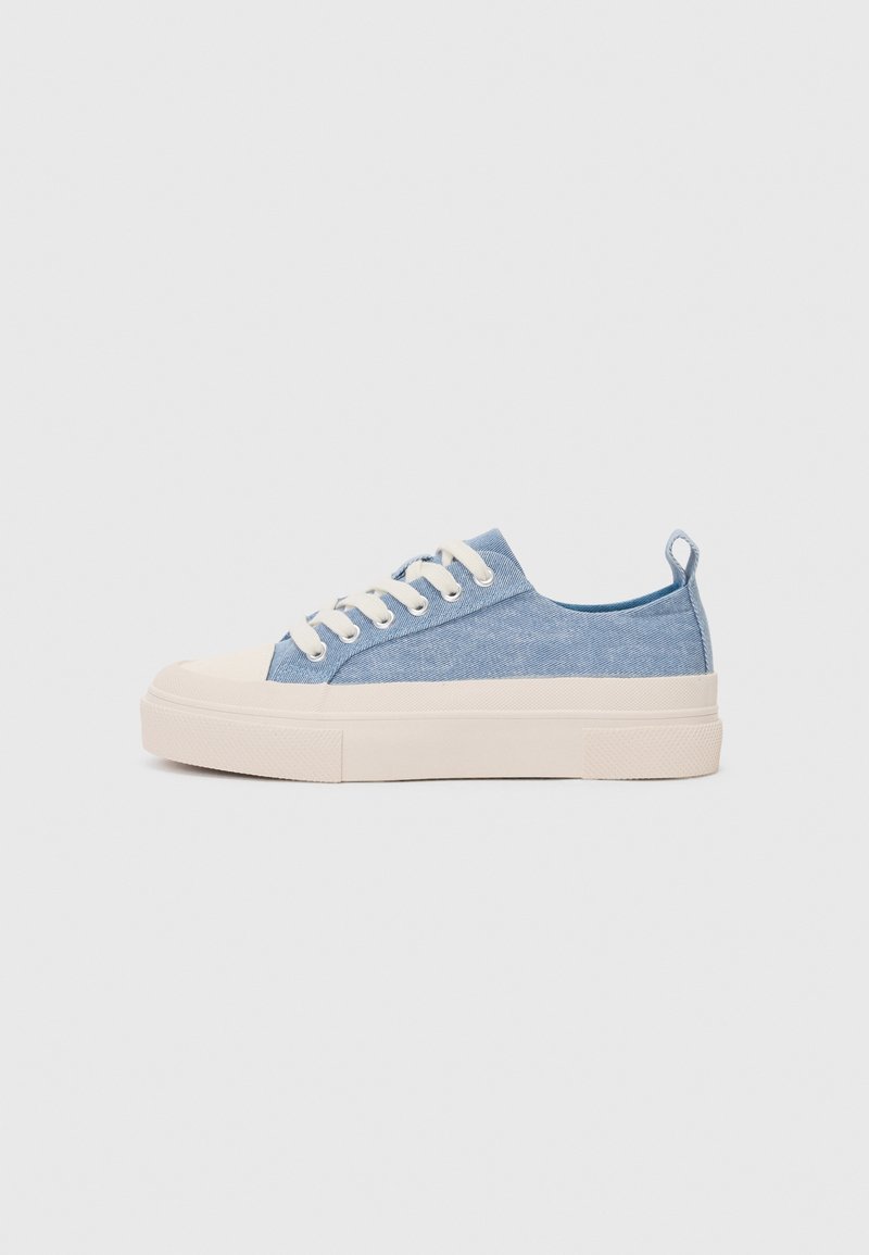 Light blue canvas sneakers with a cream rubber toe cap and outsole, featuring white laces and a pull tab on the heel.