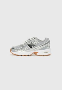 Silberner Sportschuh aus Meshmaterial, mit schwarzen Akzenten und einer Gummisohle. Verfügt über durchbrochene Details und "ABZORB"-Branding an der Ferse.