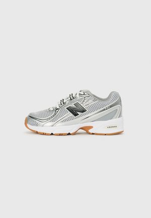 Chaussure de sport argentée avec un matériau en mesh, des accents noirs et une semelle en caoutchouc. Présente des détails perforés et le logo "ABZORB" sur le talon.