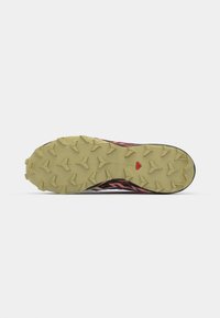 Trail running shoe sole with a textured rubber surface. Features multiple traction lugs, primarily in yellow, with a black and pink upper outline.