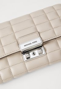 Clutch in pelle beige con design trapuntato, dotato di una chiusura in argento con una serratura e logo. La texture è liscia con dettagli di cucitura fine.