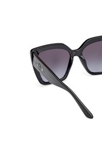 Black, oversized cat-eye sunglasses with gradient lenses. Shiny plastic frame, accentuated by branding on the temple and smooth finish.