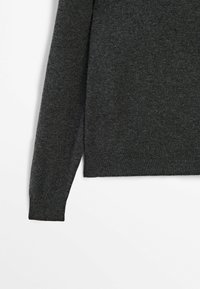 Manche de pull en maille gris foncé et partie inférieure du corps sur fond blanc.
