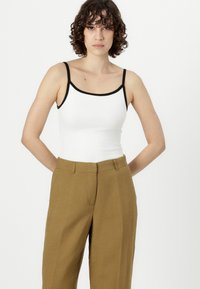 Top blanco sin mangas con detalles negros, combinado con pantalones de pierna ancha de cintura alta en color marrón claro. Textura suave y diseño minimalista.