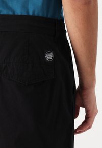 Black shorts made of fabric with a back pocket and a black circular logo patch labeled "Santa Cruz." The waistband is plain and dark.