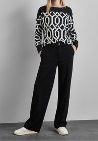 Svart och vit geometrisk mönstrad tröja med långa ärmar, kombinerad med högmidjade svarta byxor. Skorna är vita med minimal detaljdesign.