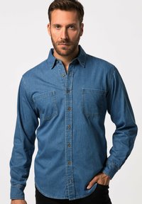 Denim-paita keskisinisessä, pitkät hihat, kaksi rintataskua, nappisulku ja kontrastiset ruskeat napit. Sileä pinta, klassinen istuvuus.