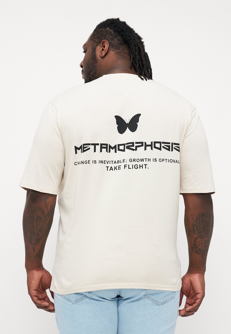 Kreminės spalvos t-shirt marškiniai, pagaminti iš minkštos medžiagos, su dideliu juodu drugelio grafiniu vaizdu ir tekstu ant nugaros, parašytu ryškia tipografija.