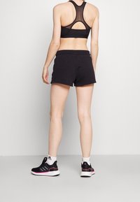 Svart sportbh med meshrygg, tillsammans med svarta shorts. Modellen bär svarta träningsskor med rosa detaljer och vita strumpor.