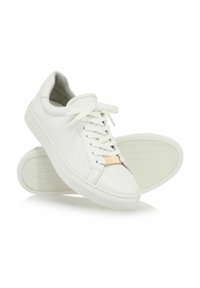 Białe skórzane sneakersy z płaskimi sznurówkami, złotymi akcentami oraz gumową podeszwą z wzorem w zygzak. Lekko zaokrąglony design noska.