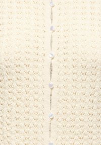 Gros plan d’un tissu tricoté couleur crème avec une rangée verticale de petits boutons ronds blancs au centre.