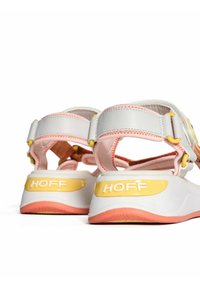 Sandalias blancas y rosa claro con un acabado texturizado, correas ajustables y un detalle de logo amarillo en el talón.