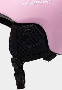 Pink helmet with a smooth surface, black mesh padding, adjustable straps, and a prominent logo. Features a secure fastening mechanism.