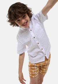 Chemise en lin blanche à manches courtes avec des boutons marron et une poche poitrine, associée à un short orange avec un motif de poissons en crème.