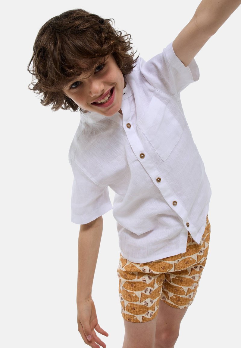 Chemise en lin blanche à manches courtes avec des boutons marron et une poche poitrine, associée à un short orange avec un motif de poissons en crème.