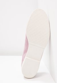 Chaussure en daim rose avec une semelle en caoutchouc blanc texturée, présentant un bout arrondi et un design minimaliste sans éléments métalliques visibles ni accents.