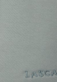 Ljusblått stickat tyg med en slät struktur, med broderad text längst ner. Designen är minimalistisk och enhetlig.