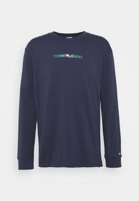 Marinblå långärmad t-shirt i bomull med broderad "TOMMY JEANS"-logotyp i grönt och rött. Rund halsringning och ribbade manschetter.