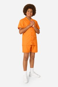 Fel oranje shirt met korte mouwen en korte broek van lichtgewicht stof, gecombineerd met witte sneakers en witte sokken tot net onder de knie.