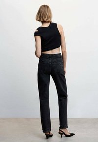 Top corto negro sin mangas con corte en los hombros, combinado con jeans negros de tiro alto con dobladillos deshilachados y zapatos de tacón negro puntiagudos.