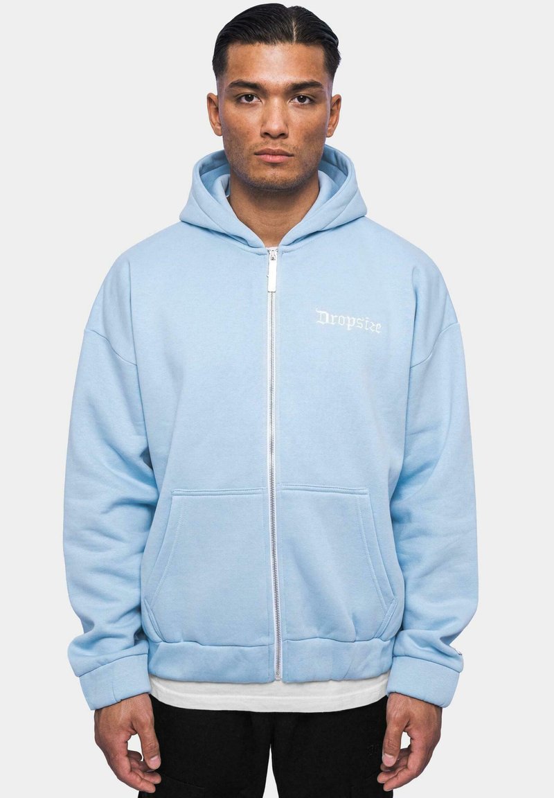 Light blue zip-up hoodie featuring a kangaroo pocket, ribbed cuffs, and a white printed logo on the left side. Soft, textured fabric.