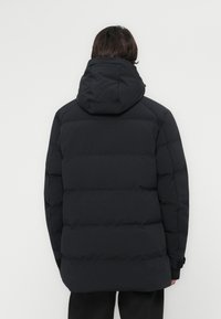 Chaqueta acolchada negra con capucha, diseño de acolchado horizontal, bolsillos laterales y puños elásticos. La tela tiene una textura suave y mate.