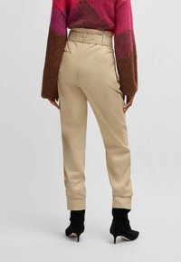 Beige højtaljede bukser med en tapered benprofil, der har en bælte detalje og manchetter, parret med sorte stiletto ankelstøvler.