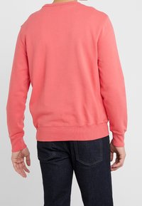 Koraal sweatshirt met lange mouwen, ribgebreide halslijn en manchetten, zachte stof en een relaxte fit, gecombineerd met donkere jeans.