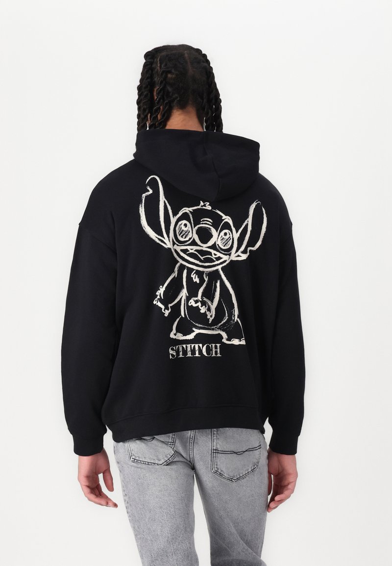 Hoodie noir en coton avec un grand graphisme blanc de Stitch, un personnage de dessin animé, au dos, accompagné du texte "STITCH" en dessous.