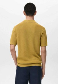 Polo a manica corta giallo senape con trama a coste e colletto a pieghe, caratterizzata da un design aderente e un motivo a maglia sottile.