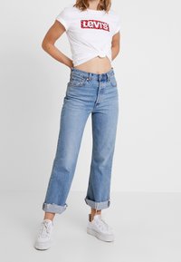 T-shirt grafica bianca con logo rosso Levi's, abbinato a jeans chiari a vita alta. I jeans hanno gamba dritta e orli arrotolati.