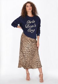 Marineblauwe sweatshirt met witte parelachtige letters met de tekst "Girls Don’t Cry", gecombineerd met een midi rok met luipaardprint en transparante sandalen met hak.