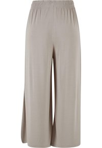 Pantalon beige clair à jambes larges avec ceinture élastique et fentes latérales, fabriqué en tissu doux et fluide.