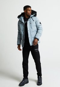 Šviesiai mėlynas pūkų striukė su kailių pamuštu kapišonu, užtrauktuku ir juodais akcentais. Suderinta su juodomis sportinėmis kelnėmis ir sportiniais batais.