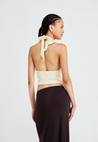 Crème haltertop met een strik bij de hals, gecombineerd met een aansluitende bruine rok. Gladde stoftextuur, minimalistisch ontwerp, open rugdetail.