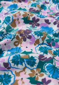Multicolored floral fabric featuring purple, blue, pink, and green flowers on a white background, with a smooth, soft texture.