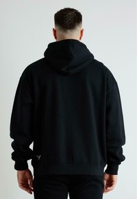 Černá mikina s kapucí vyrobená z bavlněné směsi. Obsahuje žebrované manžety a spodní lem, klokaní kapsu a decentní logo poblíž spodního lemu.