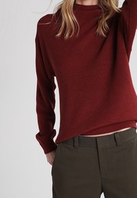 Geribbelde, kastanjebruine trui met een hoge hals en lange mouwen, gecombineerd met donkergroene broek, met een losse pasvorm en een gestructureerde stof.