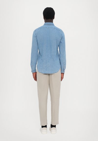 Light blue denim shirt with long sleeves, pointed collar, and buttoned cuffs, paired with light beige trousers and white shoes.
