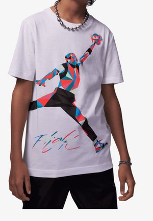 Persoon die een wit overhemd draagt met kleurrijke geometrische basketbalspelerafbeelding en gestileerd handschrift eronder, gecombineerd met een zwarte broek en zilveren ketting.